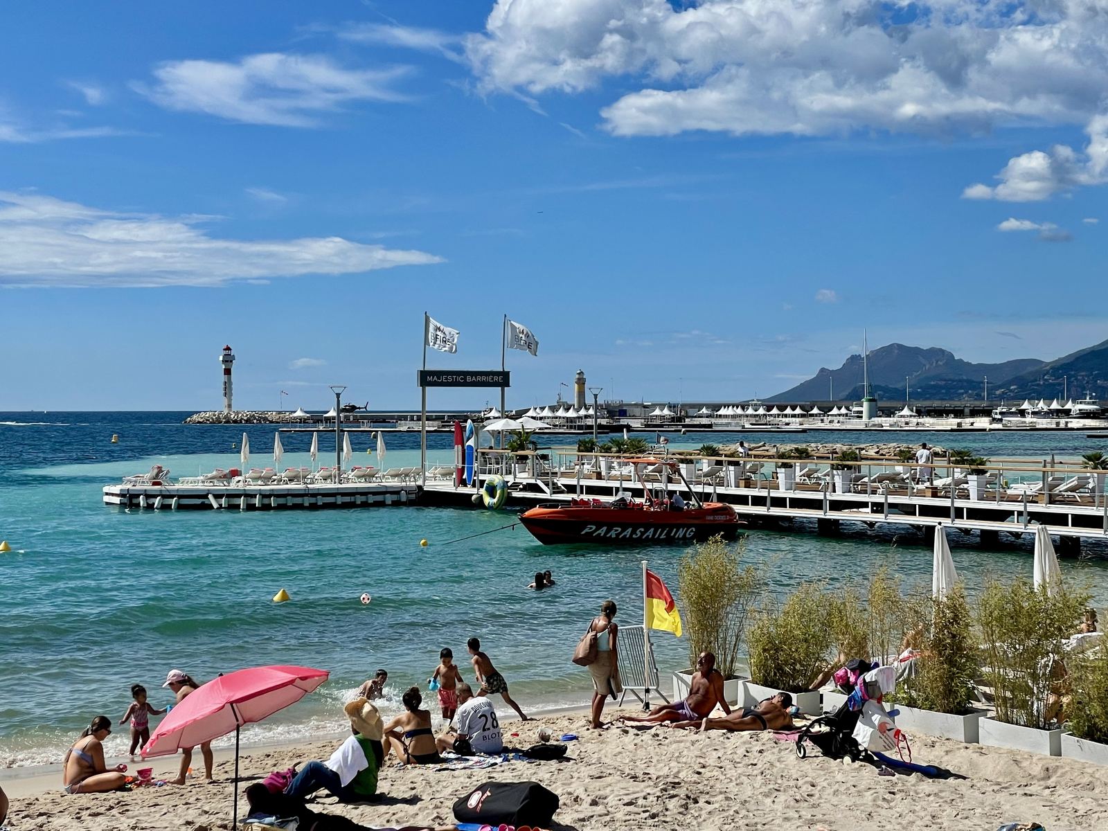 Cannes beach — the Majestic Barrière pier, red parasailing boat, people on the sand, Mediterranean behind